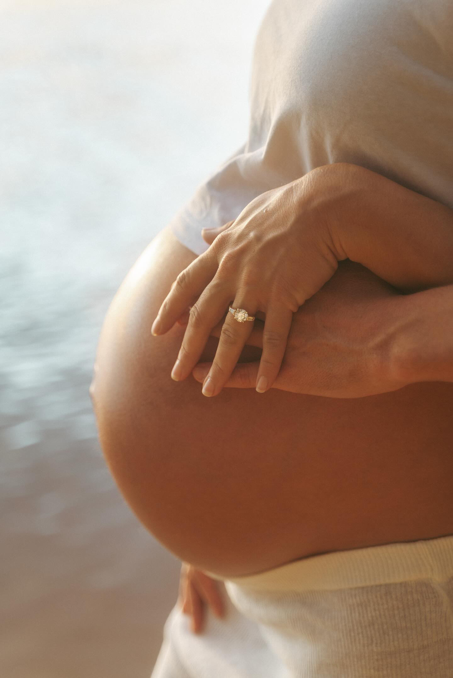 Woman's pregnant belly showing off her engagement ring and holding her partner's hand