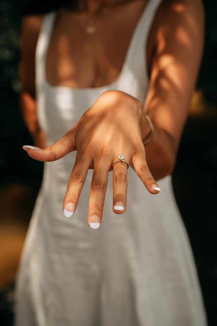 bride showing off her engagement ring wearing a white summer dress